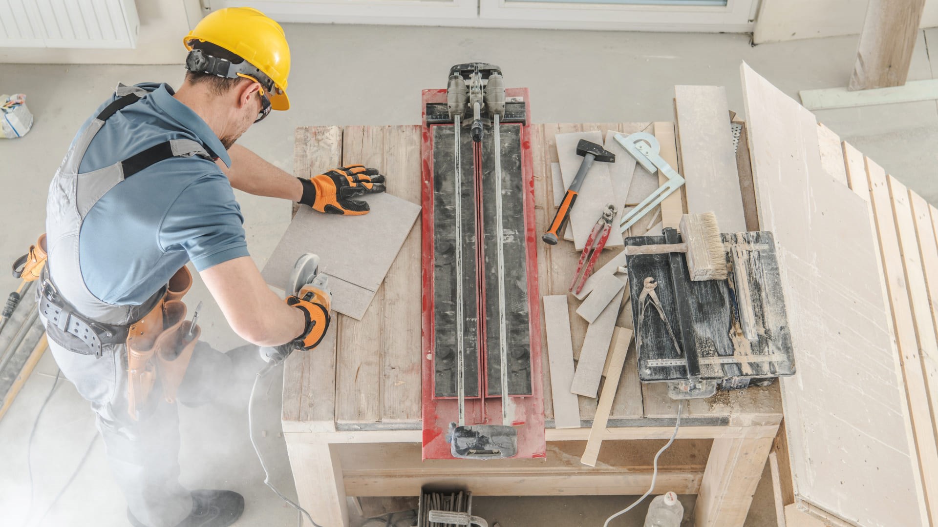 Ouvrier découpant une dalle sur un chantier intérieur avec un outil électrique, entouré d’équipements de construction.